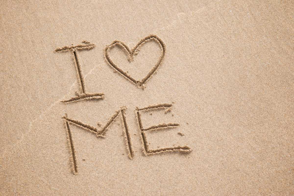 Blog Post is Affirmations for Self-Love. Image is the writing, "I heart me" written in the sand.